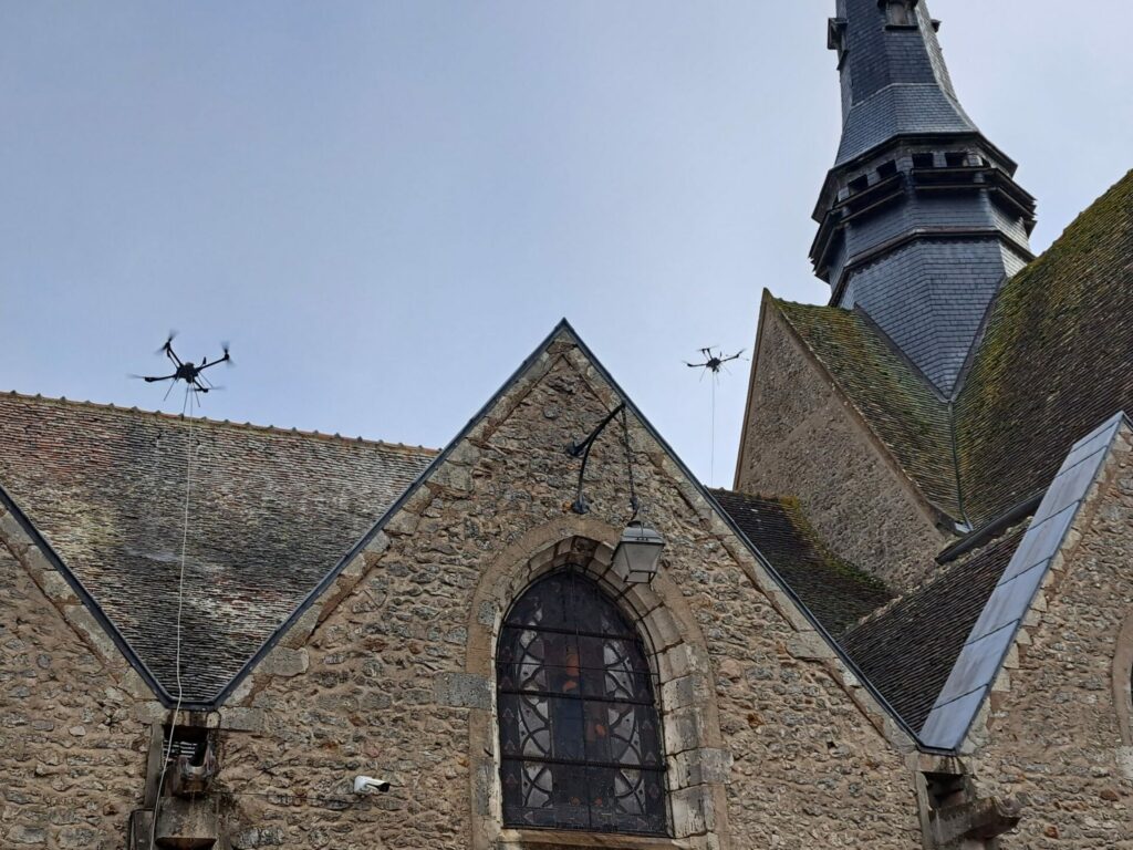 Deux drones en train de démousser al toiture d'une église